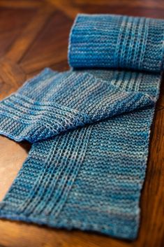 two blue knitted scarves sitting on top of a wooden table