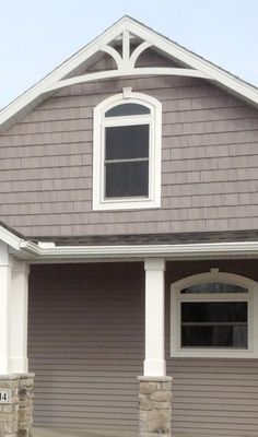 a dog is standing in front of a gray house with white trim on it's windows