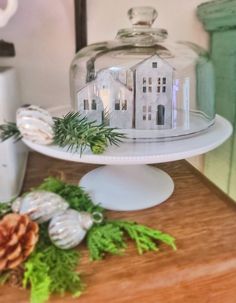 a cake plate with a house under a glass dome and pine cones on the side