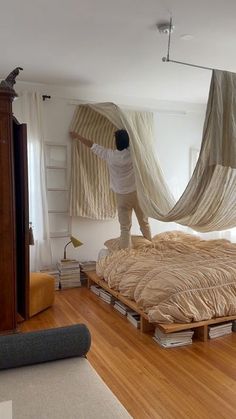 a person standing on a bed in a room with wooden floors and walls, hanging curtains from the ceiling