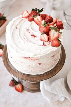 a cake with strawberries on top sitting on a wooden stand next to plates and napkins