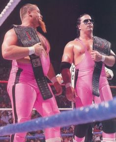 two men in pink wrestling suits standing next to each other