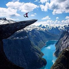 a man flying through the air while standing on top of a cliff next to a river