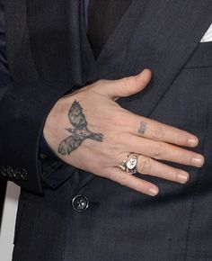 a man in a suit with a bird tattoo on his left hand, wearing a ring