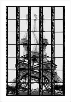 black and white photograph of the eiffel tower from behind bars in front of it