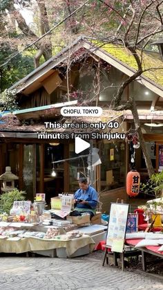 a man sitting at a table in front of a small building with lots of food on it