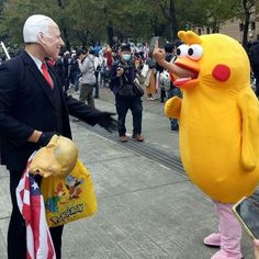 a man in a suit and tie standing next to a large yellow bird mascot with an american flag