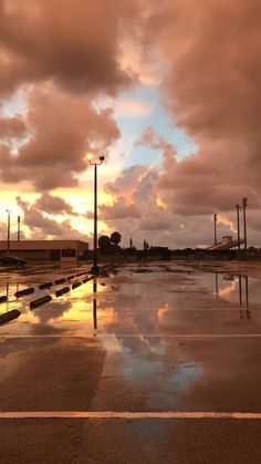 an empty parking lot with water on the ground and clouds in the sky above it