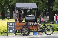 an old fashioned coffee cart is parked on the side of the road with people walking by