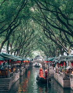 a boat is going down a canal with people on it and trees lining the sides