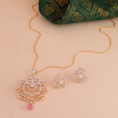 two necklaces on a pink surface next to a green bag