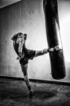 a young woman kicking a punching bag in a black and white photo, with her leg on the ground
