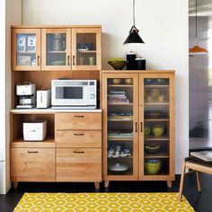 a kitchen area with a microwave, cupboards and yellow rug on the floor in front of it