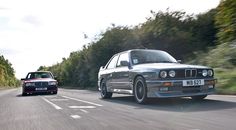 two cars driving down the road next to each other in front of trees and bushes