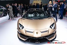 a gold sports car on display at an auto show with people standing around and looking at it