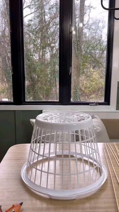 a white birdcage sitting on top of a wooden table next to a window