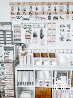 a white desk topped with lots of books and office supplies next to a wall covered in plants