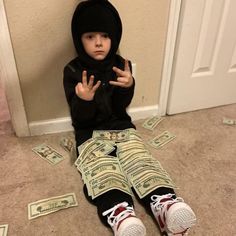 a little boy sitting on the floor with money all over his pants and hoodie