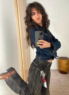 a woman in jeans is holding a cell phone and posing for the camera with her legs crossed