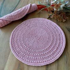 a pink crocheted rug sitting on top of a wooden floor next to dried flowers