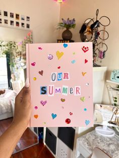 a person holding up a pink notebook with the words our summer written in colorful hearts
