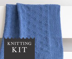 a blue knitted blanket sitting on top of a white door sill next to a sign that says knitting kit
