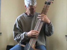 an older man sitting on a chair while holding a guitar in his right hand and looking down at the strings