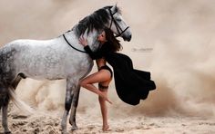 a woman is hugging a white horse in the desert with dust blowing around her behind her