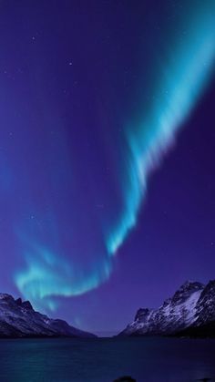 an aurora bore is seen in the night sky over water and mountains with snow on them