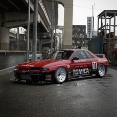 a red car parked on the side of a road next to a tall metal structure