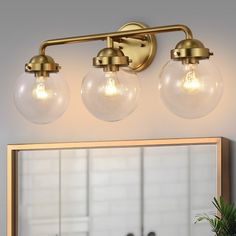 three light bathroom vanity fixture with glass globes and brass finish, in front of a mirror