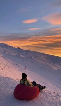 a man sitting on top of a snow covered slope next to a red sled