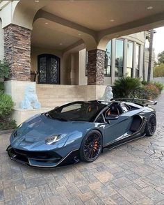 a blue and black sports car parked in front of a large house on a brick driveway