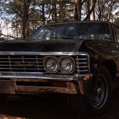 an old car parked in the woods with its hood up and headlight turned on