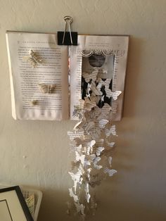 an open book is hanging on the wall next to a vase with flowers in it