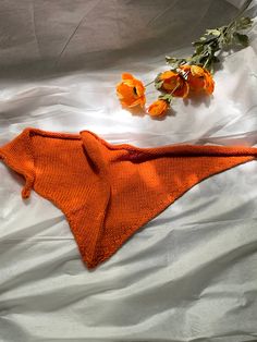 an orange knitted shawl laying on top of a bed next to some flowers