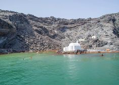 a boat is in the water near some rocks and a building with a white roof