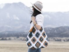 a woman carrying a crocheted purse with mountains in the background