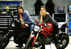 two people sitting on motorcycles in a garage