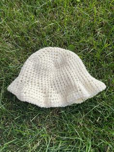 a white knitted hat laying on top of green grass in the middle of a field