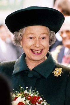 an older woman wearing a green coat and hat with flowers in her lap smiling at the camera