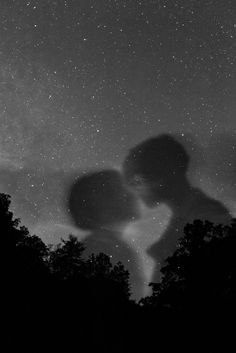 two people are kissing under the stars in the night sky with trees silhouetted against them