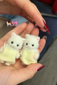 two small white kittens in yellow sweaters are being held by someone's hand