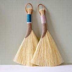 two yellow brooms are hanging on the wall with wooden handles, one has blue and pink stripes