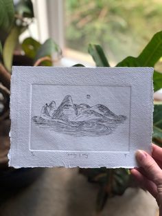 a person holding up a piece of paper that has a drawing of mountains on it