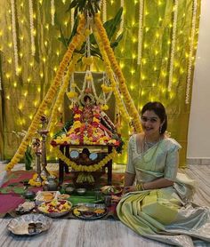 a woman sitting on the floor in front of a small shrine decorated with flowers and garlands