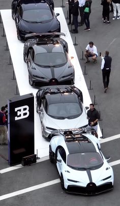 three bugatti cars are parked on a white platform as people walk by them