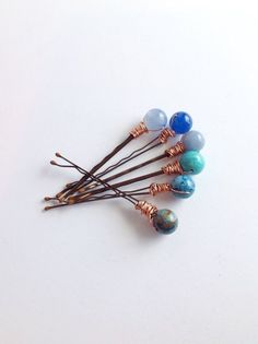 four hair pins with different colored beads and copper wire wrapped around them on a white surface