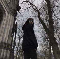 a woman standing in front of a building with trees around her and looking at the camera