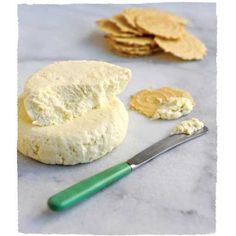 some crackers and cheese are sitting on a table with a green spatula next to them